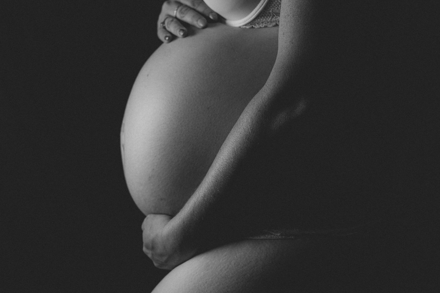 Black and white artistic photo of pregnant belly silhouetted against dark background.