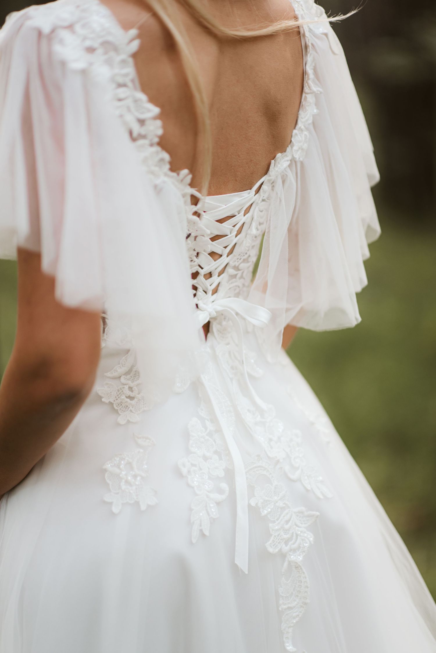 Close-up detail of white wedding dress showing lace-up back and delicate flutter sleeves.