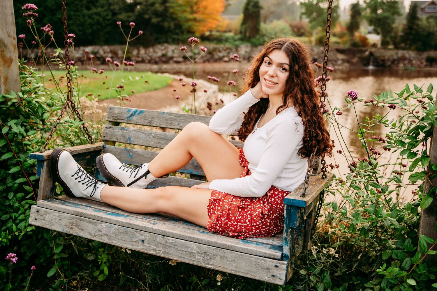 Woman in casual attire relaxes on rustic wooden bench in garden setting.