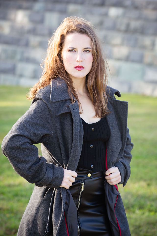 a woman is wearing a grey jacket and black skirt