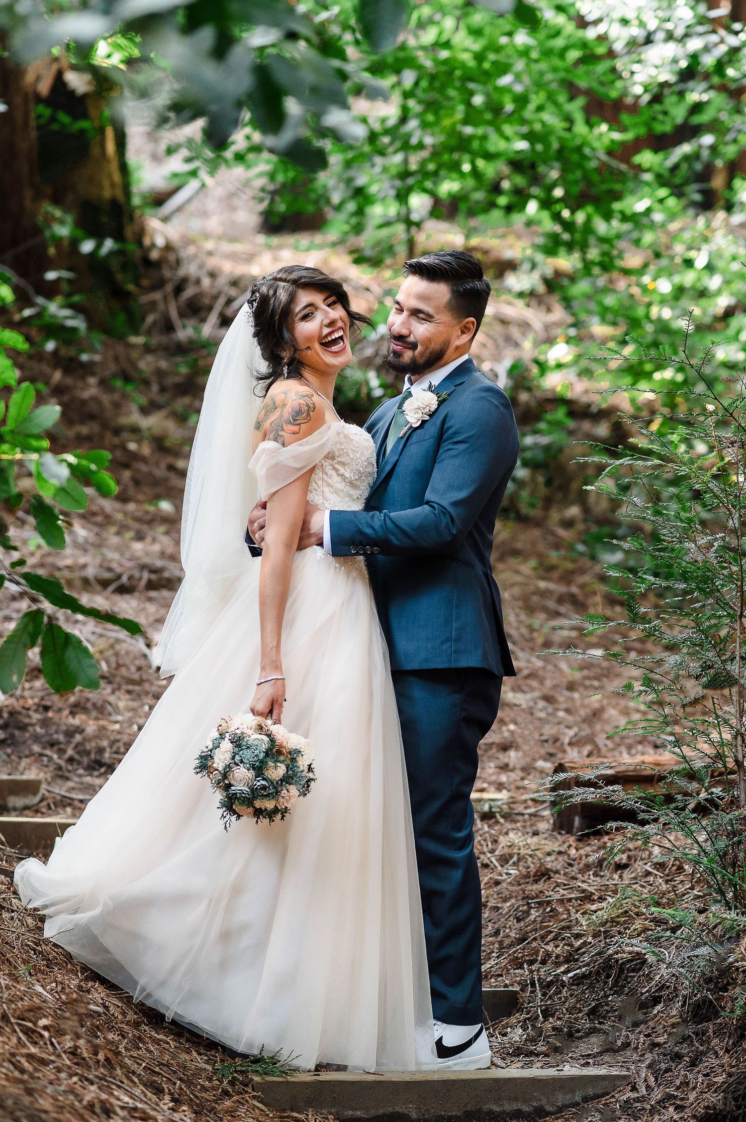 A joyful couple shares a candid moment on forest steps during their wedding photoshoot.