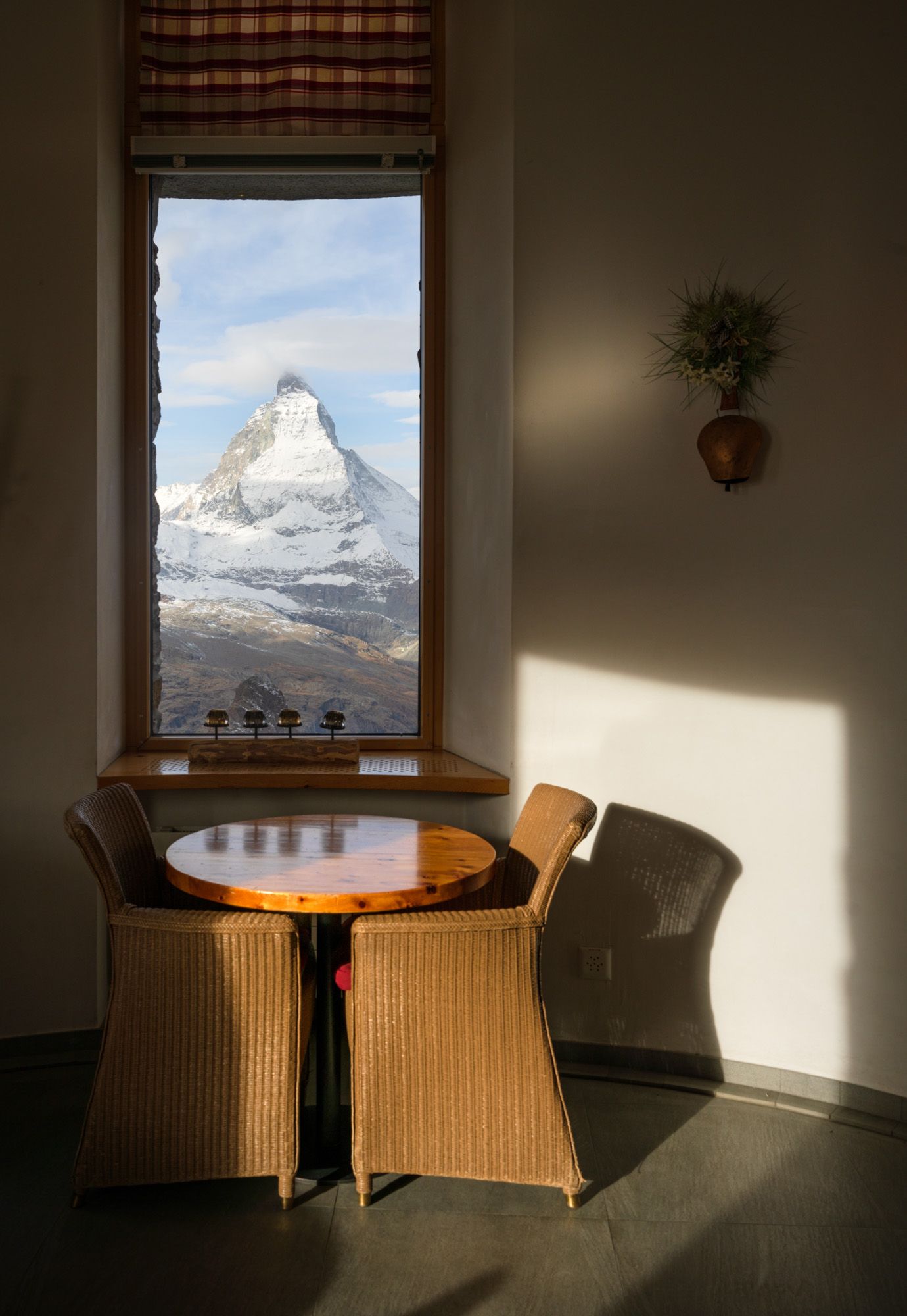 A cozy dining nook with wicker chairs offers a stunning window view of the snow-capped Matterhorn mountain peak.