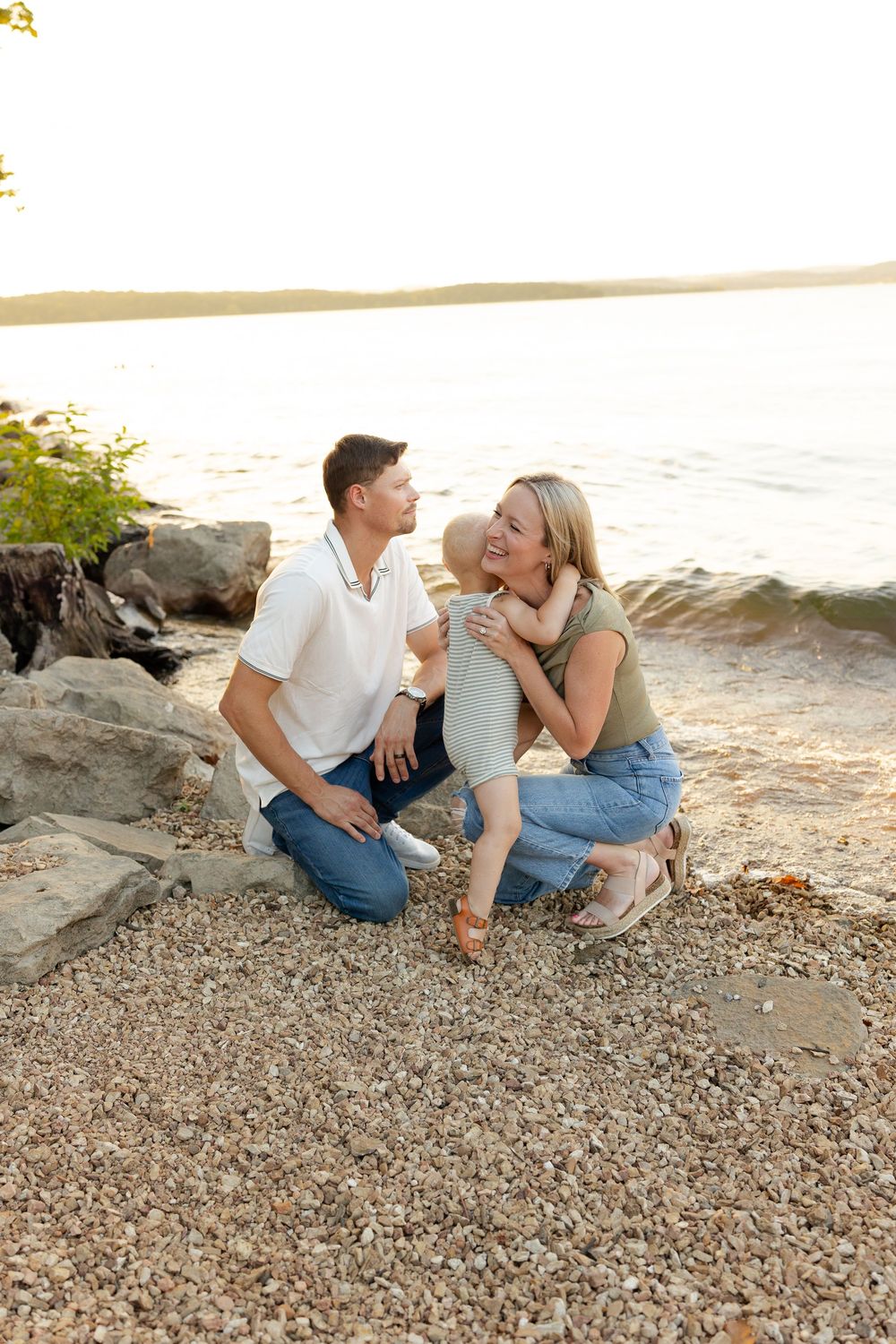 A couple sits together on a rocky beach shoreline at sunset sharing a romantic moment.