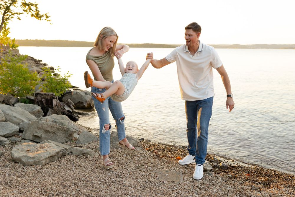 A couple holds hands while walking along a rocky beach shoreline at sunset.