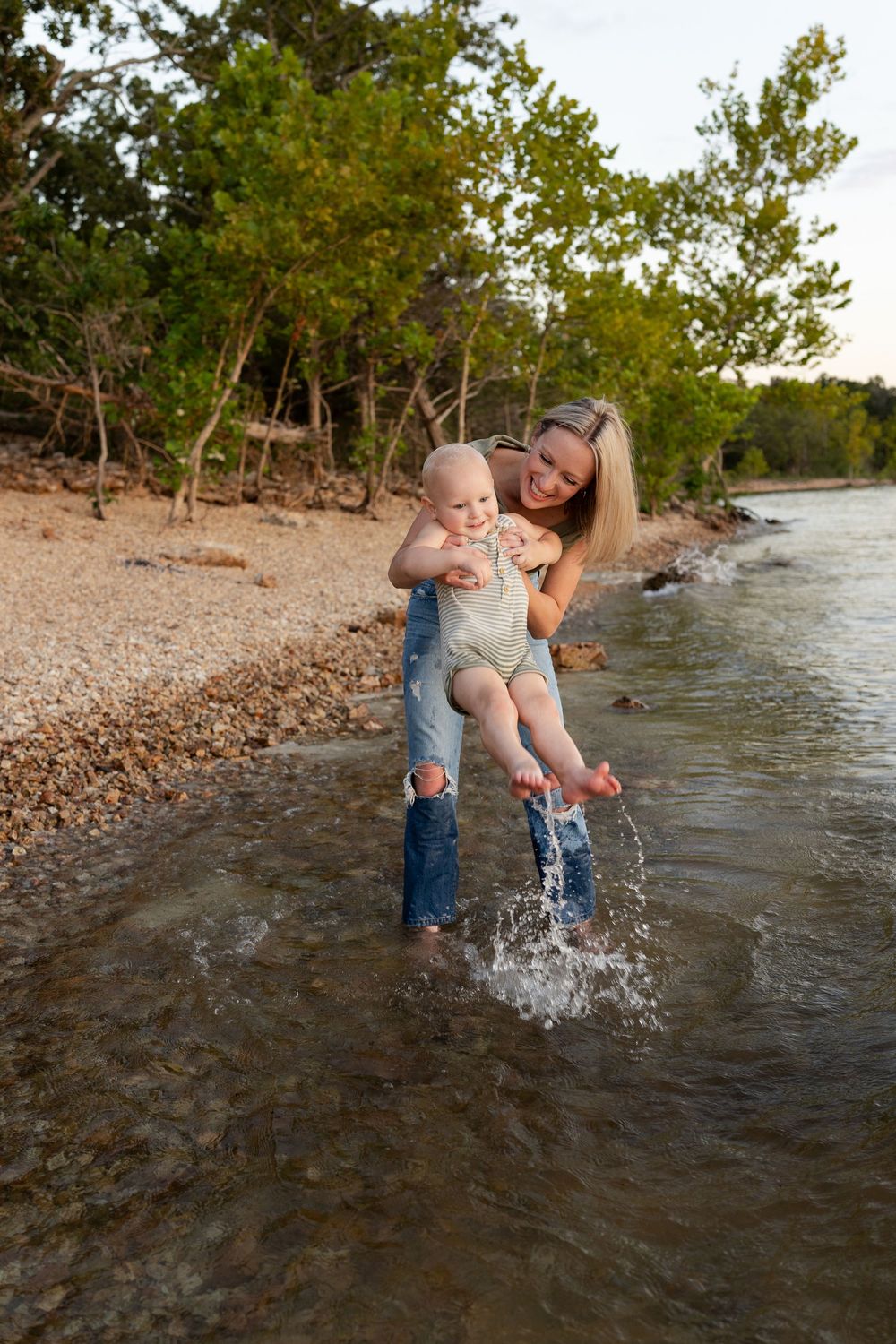 Parent and child playing together in shallow water at rocky beach, splashing and having fun on a sunny day.