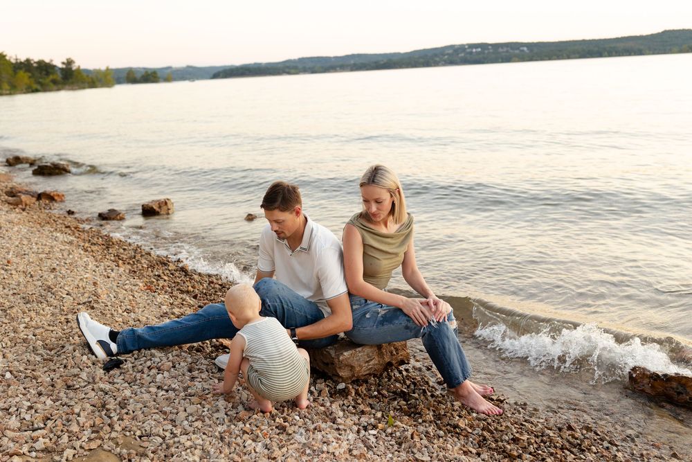 People sit along a rocky beach shoreline at sunset watching the gentle waves roll in.