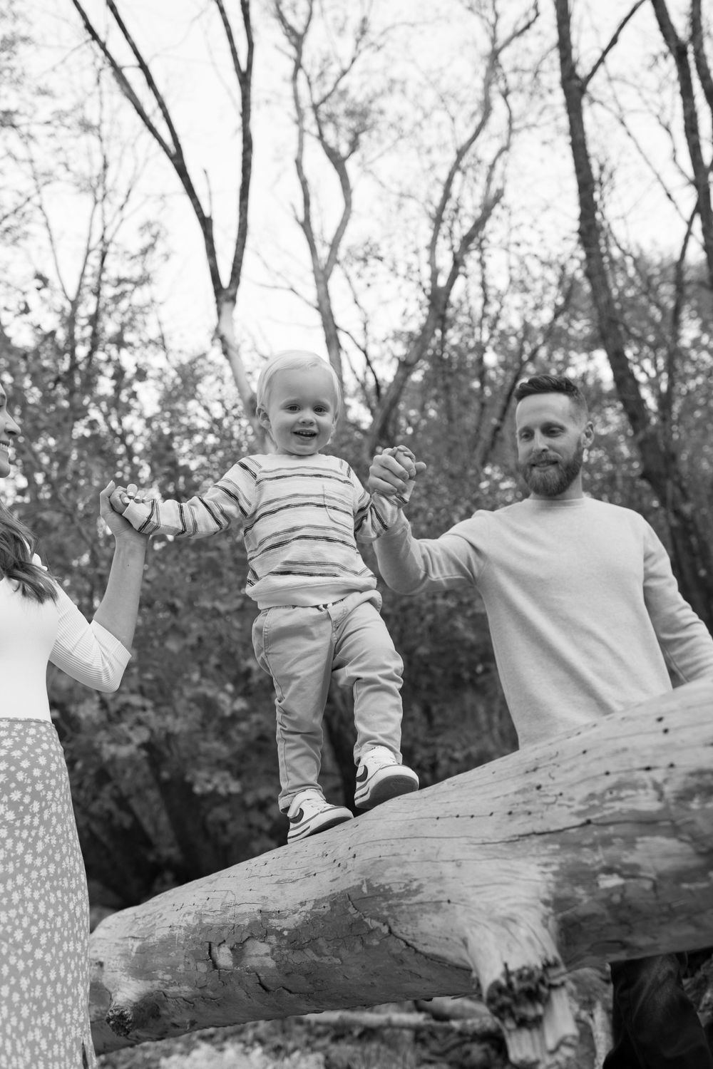 Black and white photo of family playing on fallen tree trunk in nature.