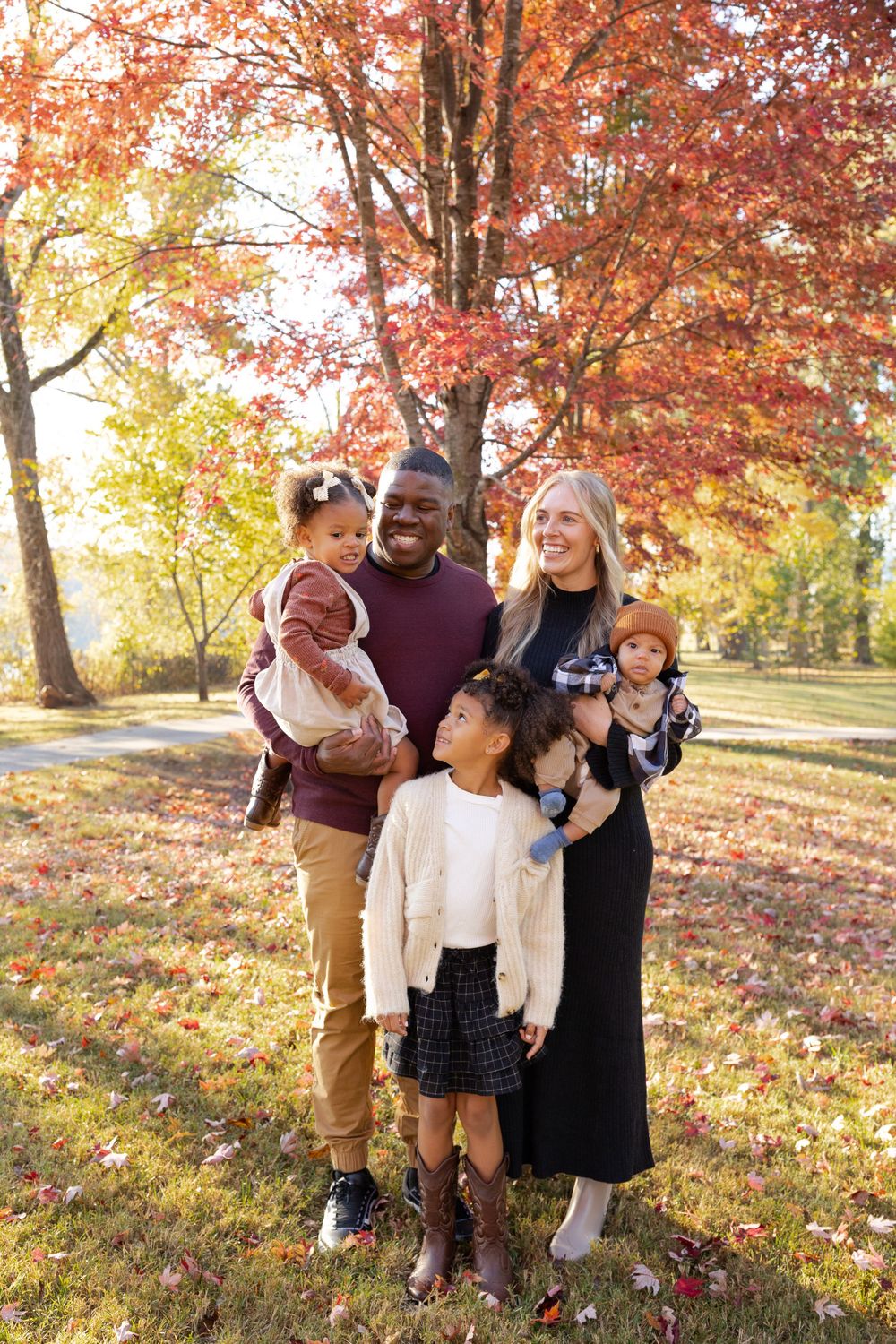 Family poses under vibrant autumn trees with fallen leaves.