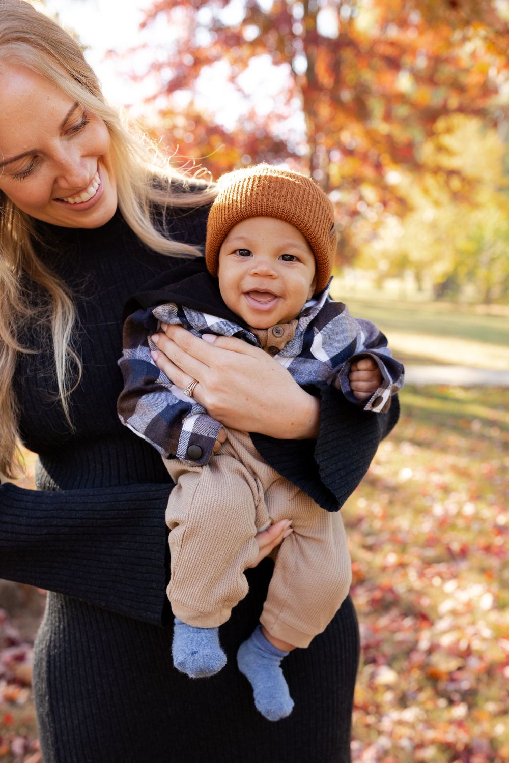 Mother and baby share joyful moment under fall foliage.