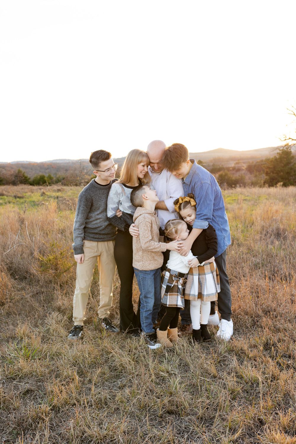 Family and dog gather close for sunset portrait in open field.