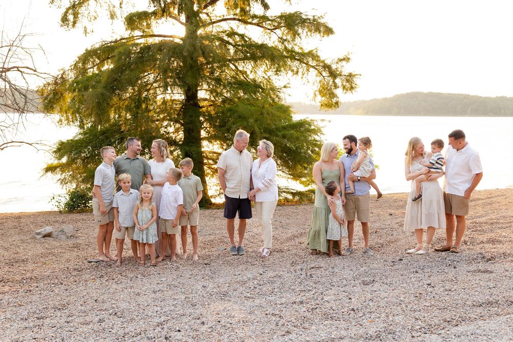 Family group in coordinated beige and white outfits walking along a rocky beach at sunset.