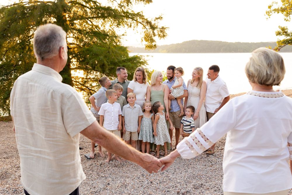 Group in white clothing holds hands in a line along a beach path during golden hour.