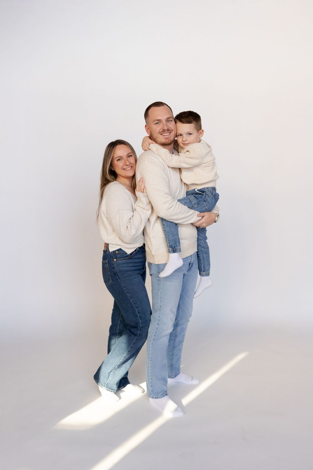 Family in matching cream sweaters poses together against white background.