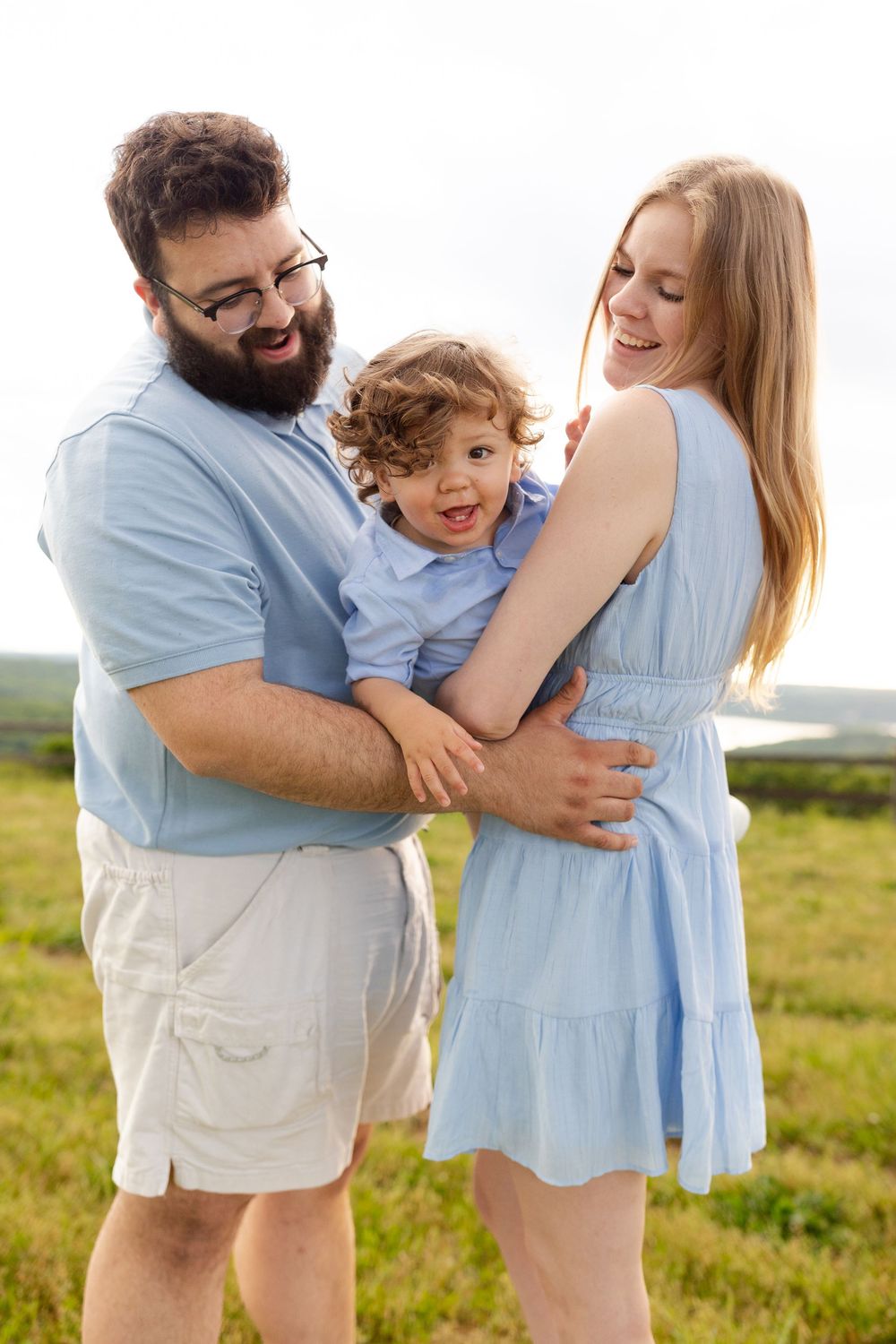 Family in coordinating blue and white outfits plays together in a sunny meadow during golden hour.