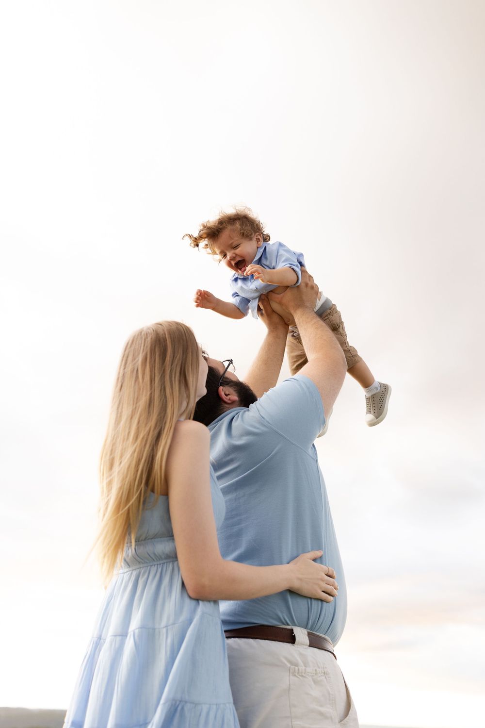 Family in light blue clothing plays together outdoors against a bright sky background.
