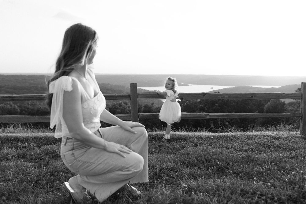 Black and white photo of women in dresses sitting in field at sunset.