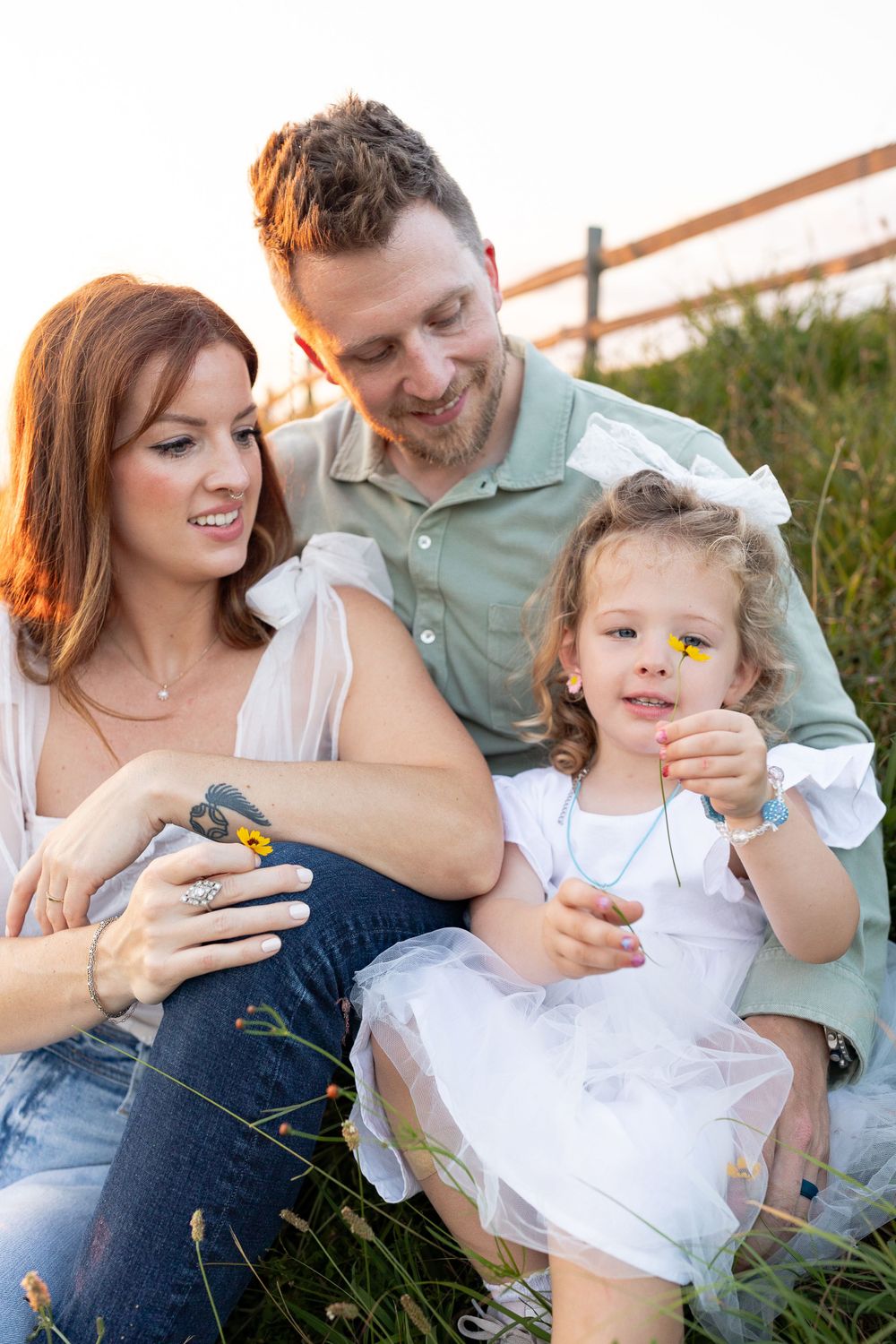 Family of three sitting on grass during golden hour photo session.