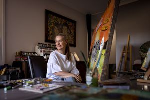 Albury Artist Kerrie Grant working in sunny studio surrounded by art supplies and painting equipment with a colorful surfboard nearby.