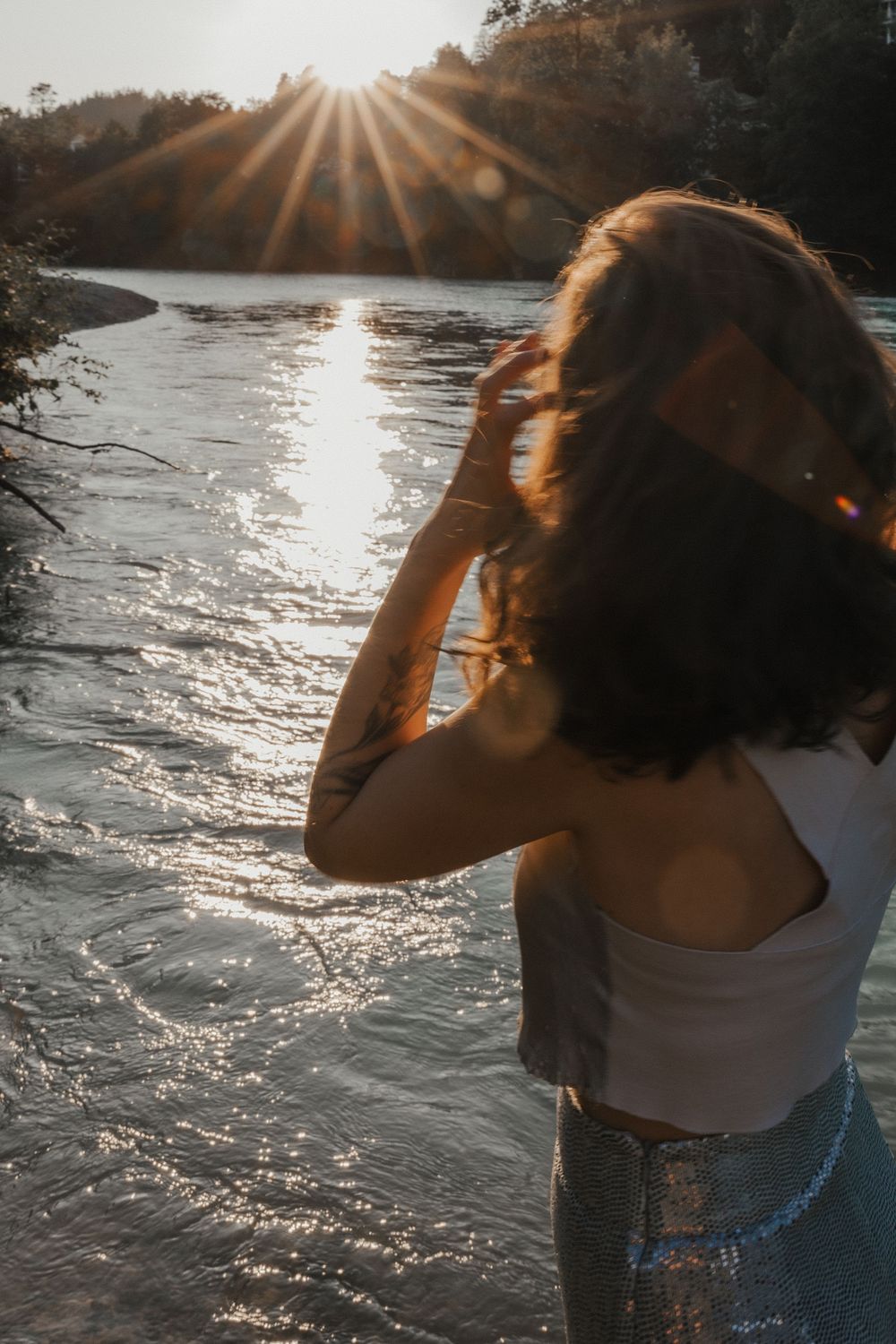 Sunlit portrait against shimmering water with dramatic lens flare and forest backdrop.