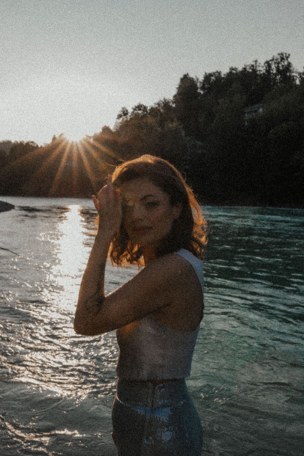 Warm-toned portrait against backlit river landscape during golden hour.