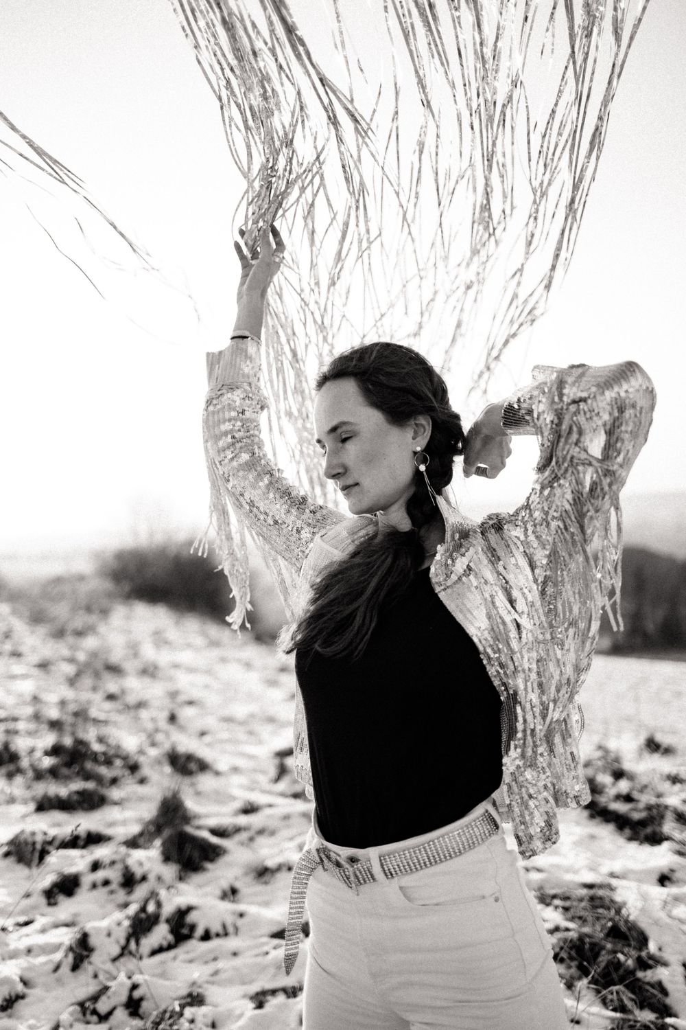 Artistic black and white portrait in snow-covered winter landscape with ethereal lighting.