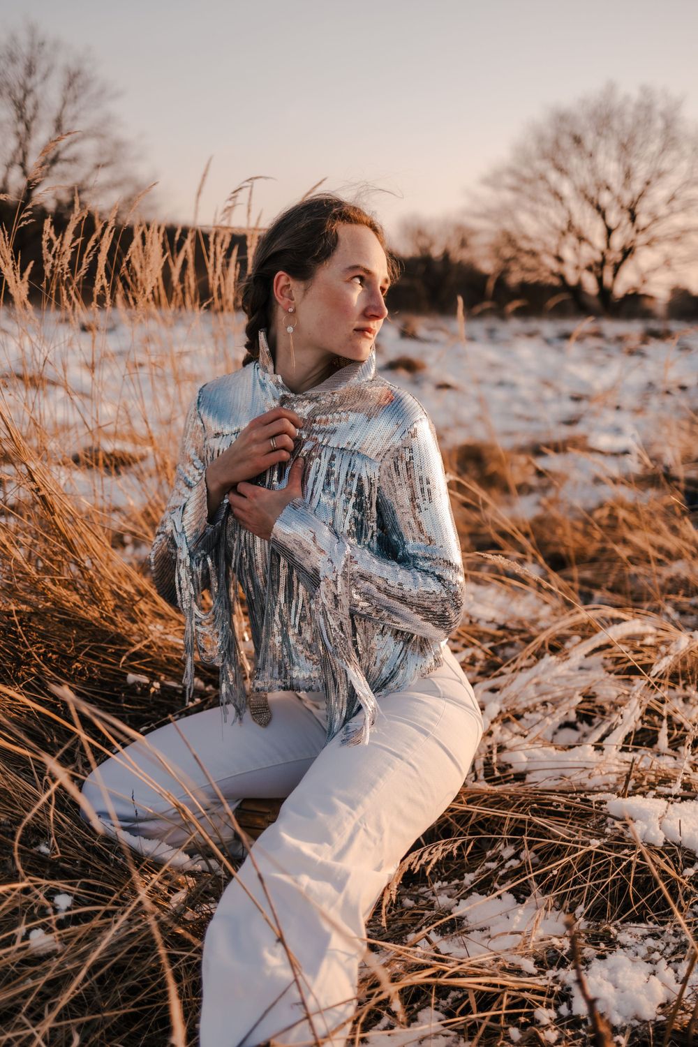 Fashion portrait in snowy field during golden hour with winter vegetation.
