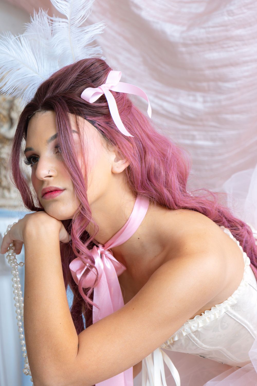 Close-up of pink-haired woman in white corset with pearl necklace and pink ribbon bow accessories.