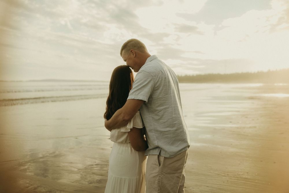 A tender embrace on a beach during golden hour with ocean waves in the background.
