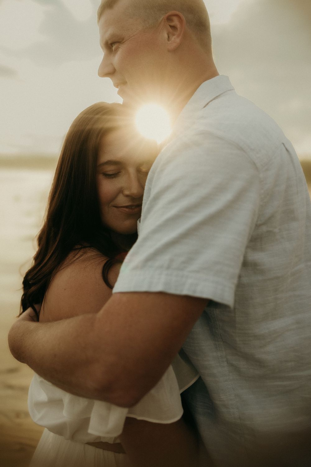 Romantic couple embracing in golden sunset light on beach with lens flare creating dreamy atmosphere.