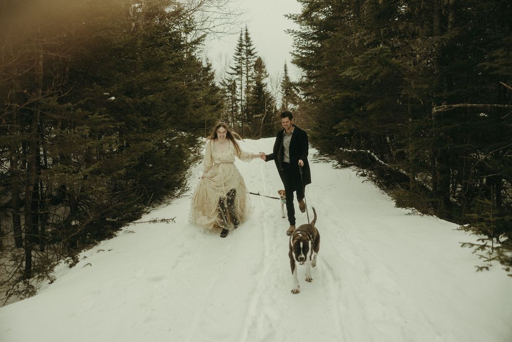 A couple walks with their dog along a snow-covered forest path.