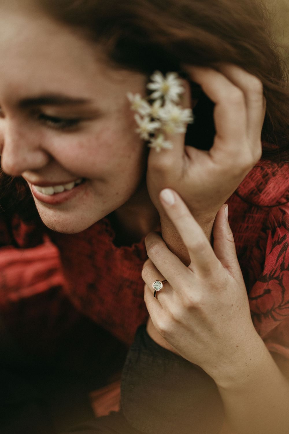 A romantic close-up shot showing a woman's smile and hand with an engagement ring in a red dress.