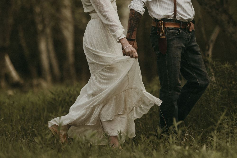 Couple in vintage attire dancing through flowering orchard.