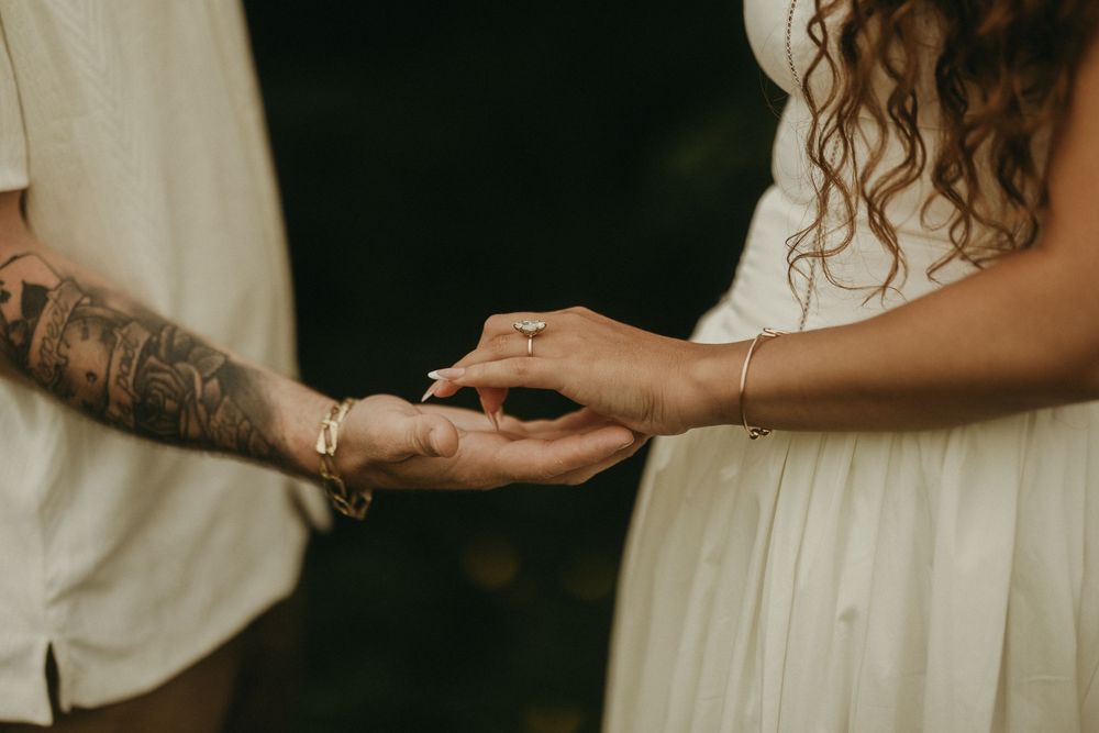 Close-up of hands with tattoos and rings showing intimate connection.