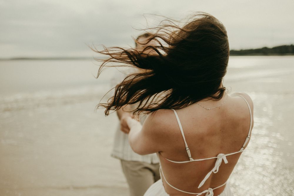 Wind blows through long hair as a couple enjoys a moment on the beach.