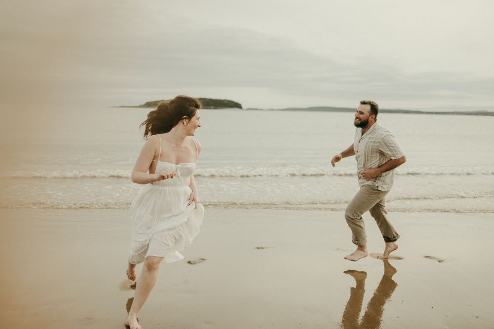 A couple runs playfully together along the beach near the ocean waves.