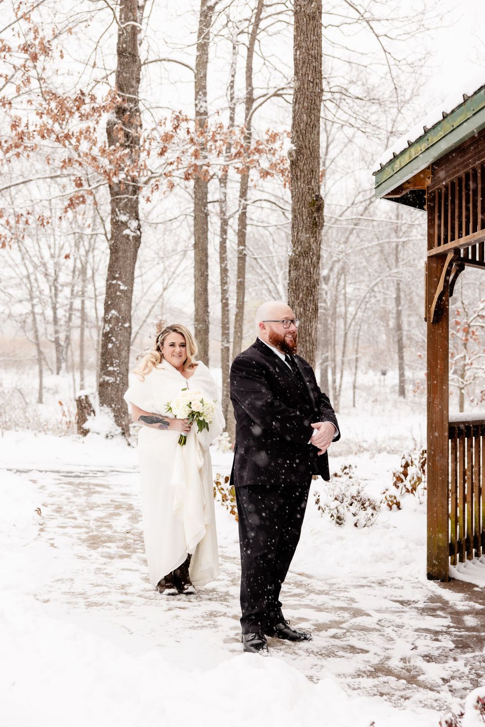 Winter wedding portraits in snowy forest with wooden gazebo backdrop.