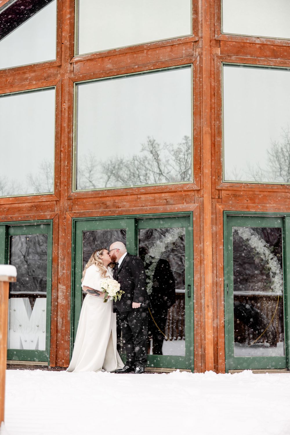 Wedding couple silhouetted against large windows in rustic wooden venue.