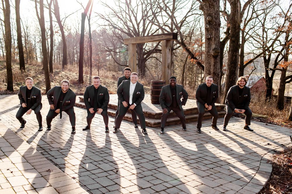Wedding party doing fun jumping poses on stone pathway surrounded by bare trees.