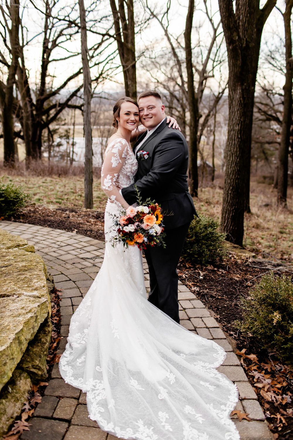 Romantic winter wedding portraits on a stone path with bare trees in the background.