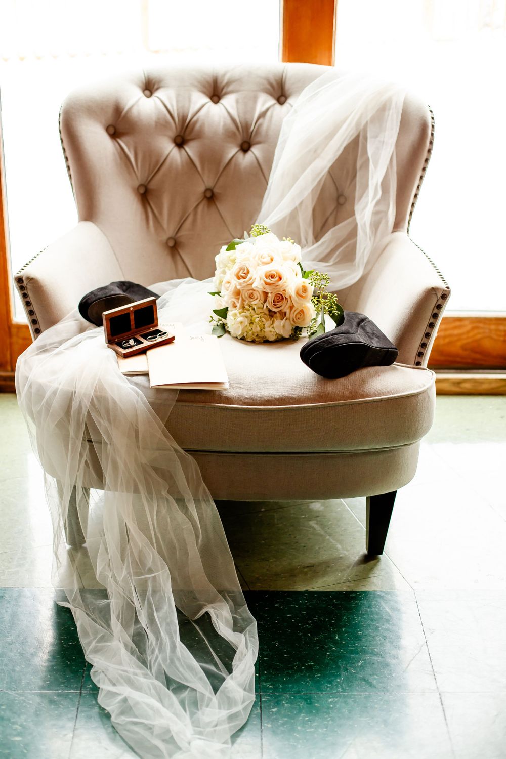 Wedding dress and accessories artfully arranged on tufted beige chaise lounge.