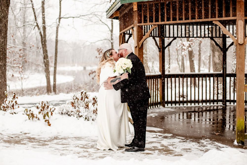 Winter wedding portraits in snow-covered gazebo surrounded by bare trees.