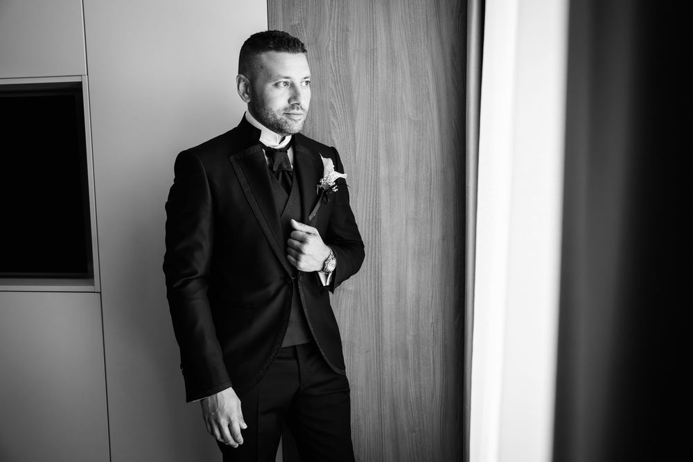 A person in a dark suit poses in a series of dramatic black and white portraits against a wooden wall.