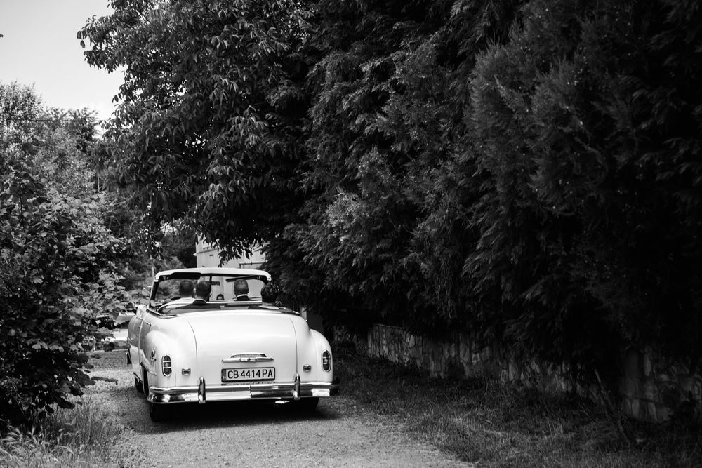 Vintage white convertible car parked on a tree-lined country road in black and white photography.