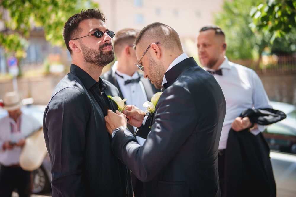 Wedding party members help adjust each other's formal attire and bowties before the ceremony outdoors.