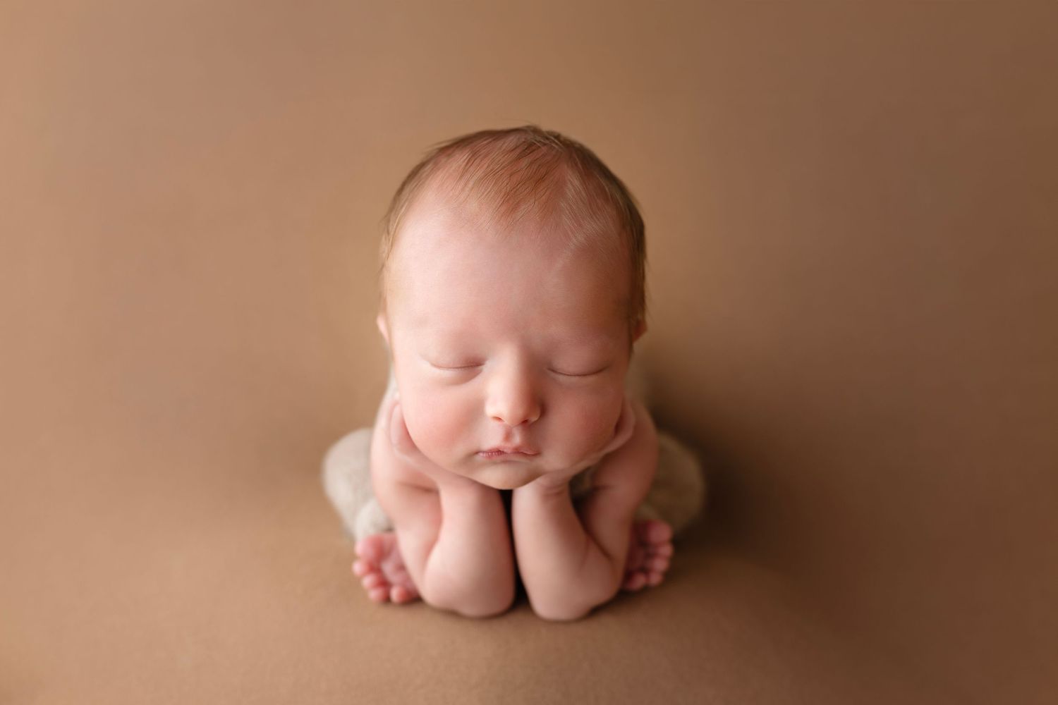 Side view of sleeping newborn in frog pose on brown backdrop.