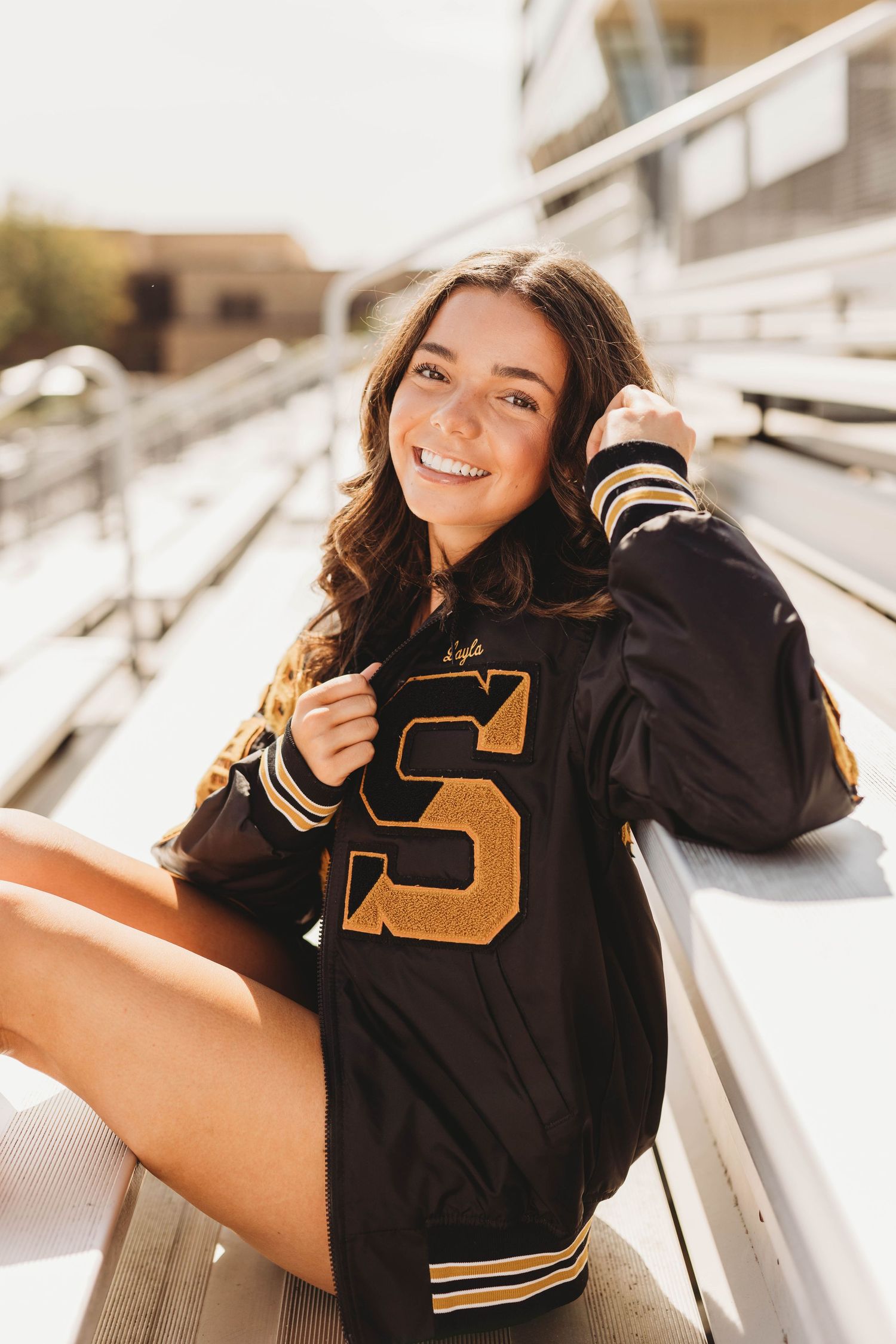 Woman in black varsity jacket poses for casual outdoor photoshoot.
