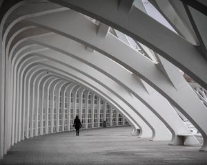 Person walking alone through futuristic white arched corridor with repeating geometric architecture.