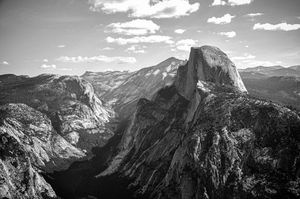 Black and white aerial view of Half Dome and Yosemite Valley mountains under a cloudy sky.