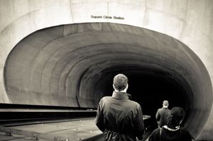 Two people on escalator descending into Dupont Circle Station tunnel in black and white.
