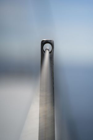 Looking up a sleek metal mast of a sailboat with a rigging hole at the top against a grey sky.